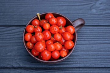 a pile of small fresh red vegetables cherry tomatoes in a brown cup on a black wooden table