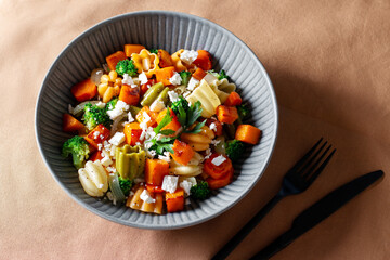 Autumn pasta salad with roasted pumpkin, broccoli, feta cheese on dark wooden background, fall season salad