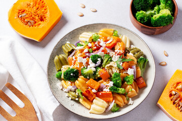 Autumn pasta salad with roasted pumpkin, broccoli, feta cheese on bright light background, fall season salad
