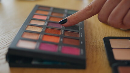 Woman finger pointing makeup palette at home close up. Girl taking eye shadows