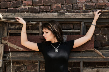 A girl dressed in a black T-shirt spread her arms, leaning her back against the old discarded doors, her gaze directed to the side. Summer walk.