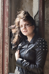 A girl dressed in a black jacket with her hair down stands near a window without glass. The wind blows from the street into an old abandoned building.