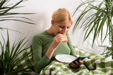 Emotionally decaying, a girl stays in bed, her day revolving around her phone and occasional bites of toast, signifying her deteriorating mental state. Bed rotting © Konstiantyn Zap