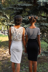 Two girls hold hands and look at the sunset. Female friend. Photograph of people from the back.