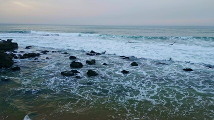 Fototapeta na wymiar Cloudy ocean splashing cliffside nature at beach closeup. Waves covering rocks