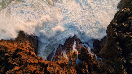Rough water breaking coast cliffs closeup. Top view foamy sea splashing rocks