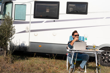 One man digital nomad lifestyle working on alternative outside workplace desk with a camper van motorhome house in background. People and office freedom. Modern small business concept job traveler