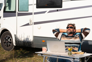 One man digital nomad lifestyle working on alternative outside workplace desk with a camper van...