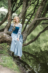 A young beautiful girl in a summer park. A beautiful medieval elf princess in a blue dress in the forest.
