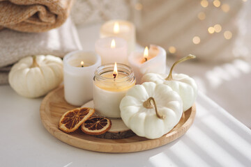 Obraz na płótnie Canvas Autumn home decor with white pumpkins and burning aroma candles with sweet spicy pumpkin pie scent. Cozy fall composition, relaxation, aromatherapy. Apartment design, living room or bedroom