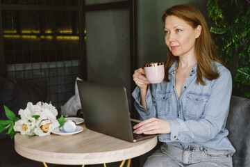Woman working on laptop in cafe. Middle-aged freelancer with cup of coffee typing and reading. Loft working place with green plants
