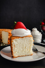 Slice of Angel Food Cake Topped with Whipped Cream and Strawberries: Piece of sponge cake on a plate with whipped topping and strawberry garnish