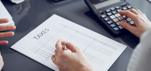Woman accountant using a calculator and laptop computer while counting taxes for a client. Business...