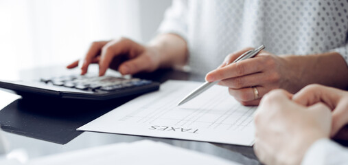 Woman accountant using a calculator and laptop computer while counting taxes for a client. Business audit and finance concepts