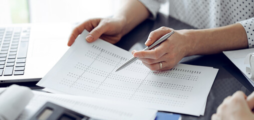 Female accountant pointing with a pen into audit paper while explaining tax counting results, close...