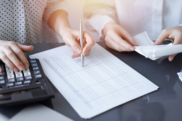 Woman accountant using a calculator and laptop computer while counting taxes with a client or colleague. Business audit team