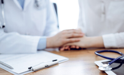 Stethoscope and tablet computer are lying on the wooden table while doctor's hands reassuring a patient at the background. Medicine concept