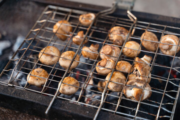 Close-up of grilled mushrooms champions in bbq grill net with hot coal underneath. Grilling cooking food outdoors in nature, simple food on weekend