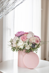 An elegant bouquet of fresh roses, peonies, and daisies in a pink box, beautifully arranged and placed by a light-filled window.