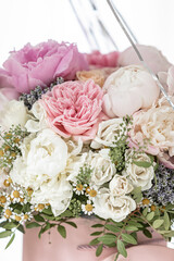 An elegant bouquet of fresh roses, peonies, and daisies in a pink box, beautifully arranged and placed by a light-filled window.