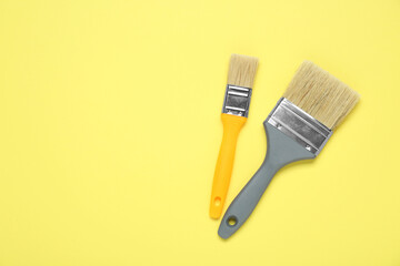 Two paint brushes on pale yellow background, flat lay. Space for text