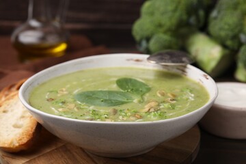 Delicious broccoli cream soup with basil and pumpkin seeds served on wooden table, closeup