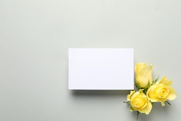 Beautiful yellow roses and blank card on light grey background, flat lay. Space for text