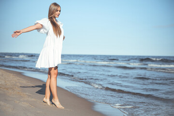Fototapeta na wymiar Happy smiling beautiful woman is walking on the ocean beach with open arms