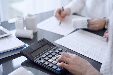 Two accountants use a calculator and laptop computer for counting taxes or revenue balance. Business, audit, and taxes concepts