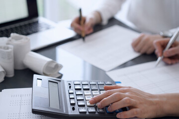 Fototapeta premium Two accountants use a calculator and laptop computer for counting taxes or revenue balance. Business, audit, and taxes concepts