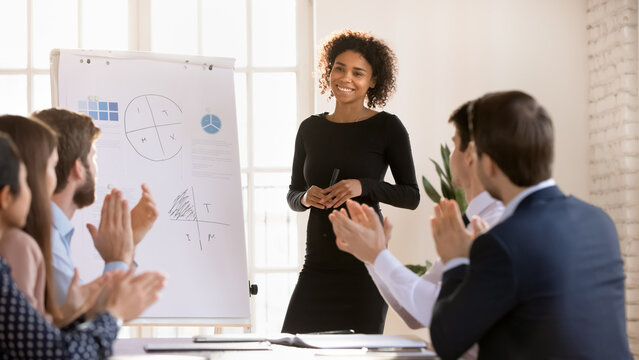Diverse team of employees applauding to positive successful speaker colleague after presentation, clapping hands at meeting table, thanking coach for seminar, lecture, business education event
