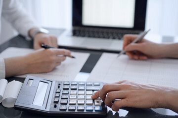 Fototapeta premium Two accountants use a calculator and laptop computer for counting taxes or revenue balance. Business, audit, and taxes concepts