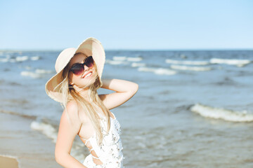 Happy blonde woman in free happiness bliss on ocean beach standing with sun glasses and hat