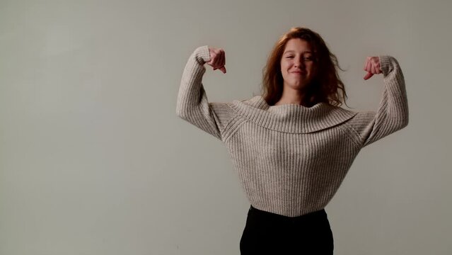 A smiling pretty girl in a mischievous and humorous mood flirts and shows off her biceps. A young comedian actress funs and makes the audience laugh at a meeting with fans. Gestures of fists and