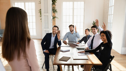 Happy diverse business team voting on presentation, raising hands at meeting table, asking...