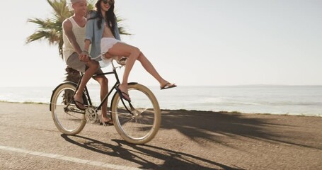 Summer, beach and a couple riding a bike together on the street for love, romance or a tropical date. Travel, smile or happy with a man and woman on a bicycle by the ocean or sea for bonding