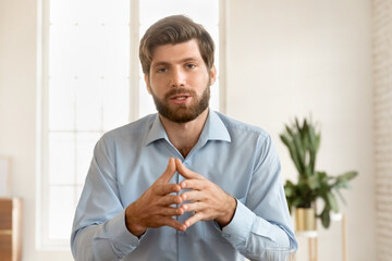 Serious handsome young business blogger man speaking at camera, giving training webinar, online...