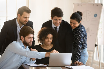 Positive multiethnic team meeting at workplace, looking at computer, pointing at laptop display, talking, discussing online project presentation, Internet startup, working in room together