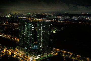 Fototapeta na wymiar Incheon City Skyline at night in South Korea, tall clusters of illuminated buildings on the dark cloudy sky with the view of Seoul over the distant mountains