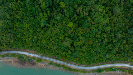 Idyllic winding road through the green pine forest. Aerial view of beautiful natural Road and green field in the wild forest mountain near Lake.