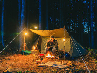 夜の森で焚き火をしながらソロキャンプを楽しむ人 - obrazy, fototapety, plakaty
