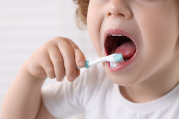 Little boy brushing his teeth with plastic toothbrush on white background, closeup