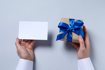Man holding gift box with blue bow and blank greeting card on white background, top view