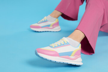 Woman wearing pair of new stylish sneakers on light blue background, closeup