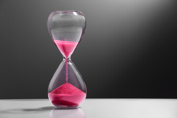Hourglass with pink flowing sand on color background. Space for text