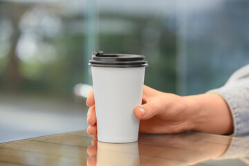 Woman holding takeaway paper cup at table, closeup. Coffee to go