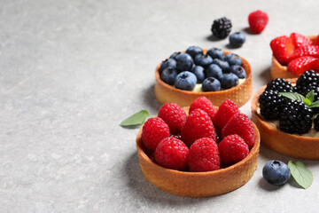 Tartlets with different fresh berries on light grey table, space for text. Delicious dessert