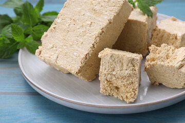Pieces of tasty halva and mint on light blue wooden table, closeup