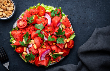 Juicy salad with watermelon, cherry tomatoes, red onion, salted peanuts and parsley, black table background, top view