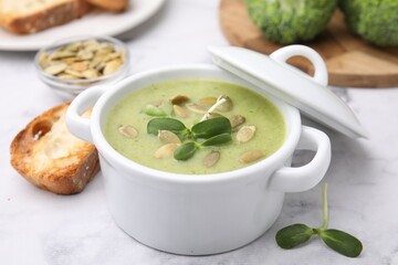 Delicious broccoli cream soup with pumpkin seeds on white marble table